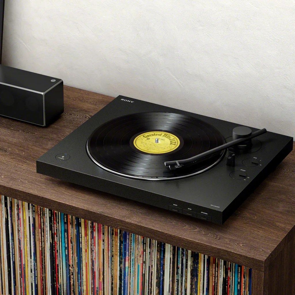 Sony turntable playing a record, placed on a wooden console with a collection of vinyl records stored underneath, next to a black speaker