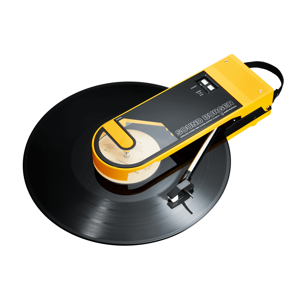 Audio-Technica SoundBurger portable record player in bright yellow, playing a black vinyl record with a compact and retro design.