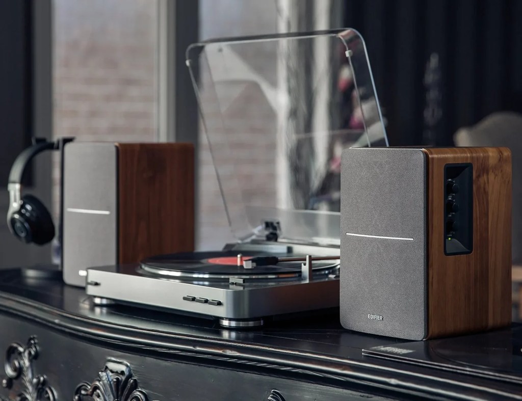 Elegant vinyl listening setup featuring a sleek turntable with a dust cover, wooden Edifier speakers, and headphones on a stand, set against a cozy living room background.