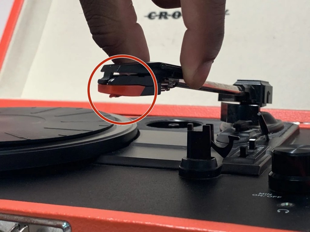Close-up of a Crosley record player needle being held above the platter, highlighting the stylus and cartridge in use.