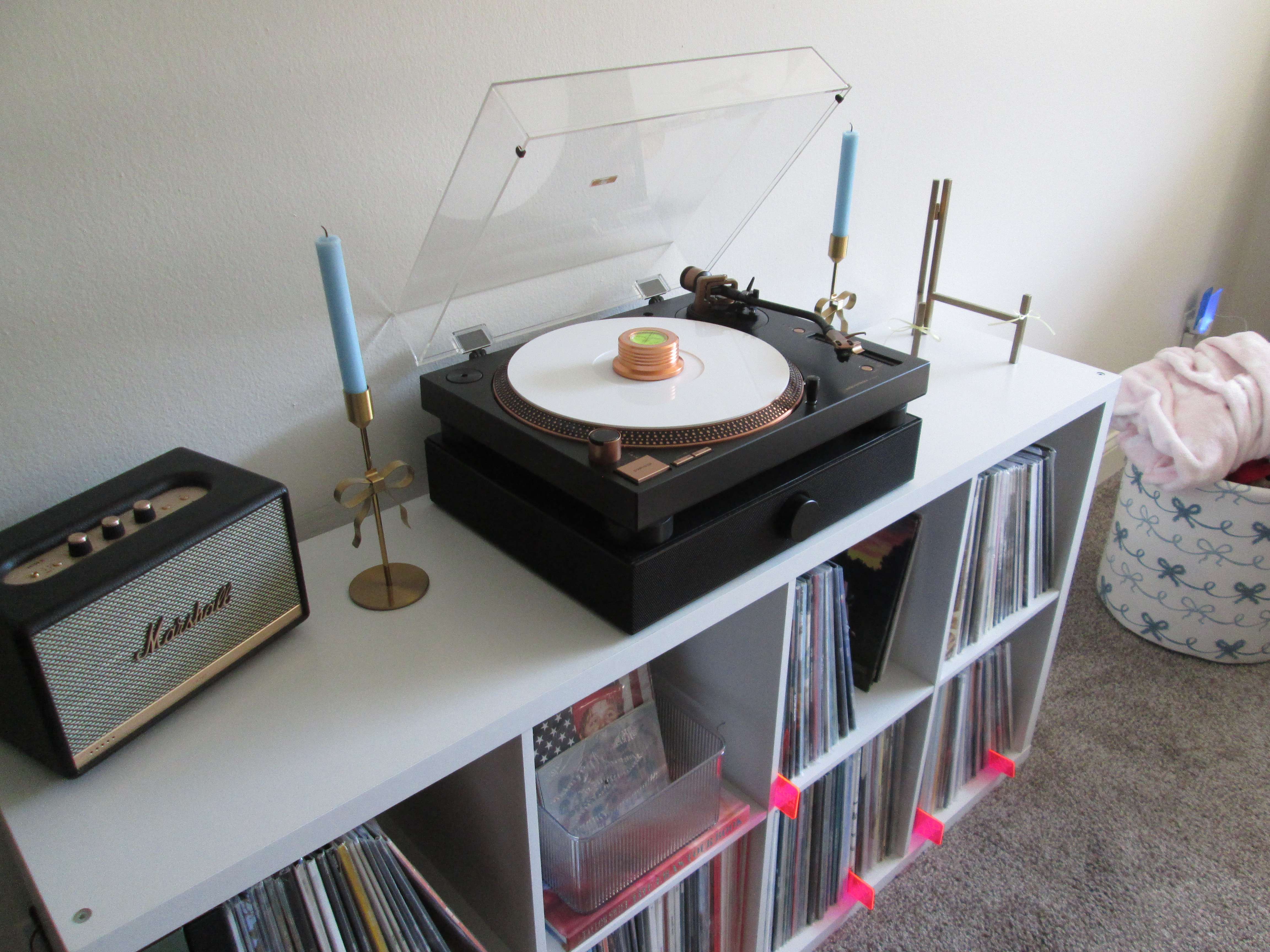 Caroline’s setup angled from the side, showcasing the bronze Audio-Technica LP120X turntable with a white record, Viborg record weight, and Spinbase speaker, next to a Marshall speaker and candle stands on top of a white vinyl shelf.