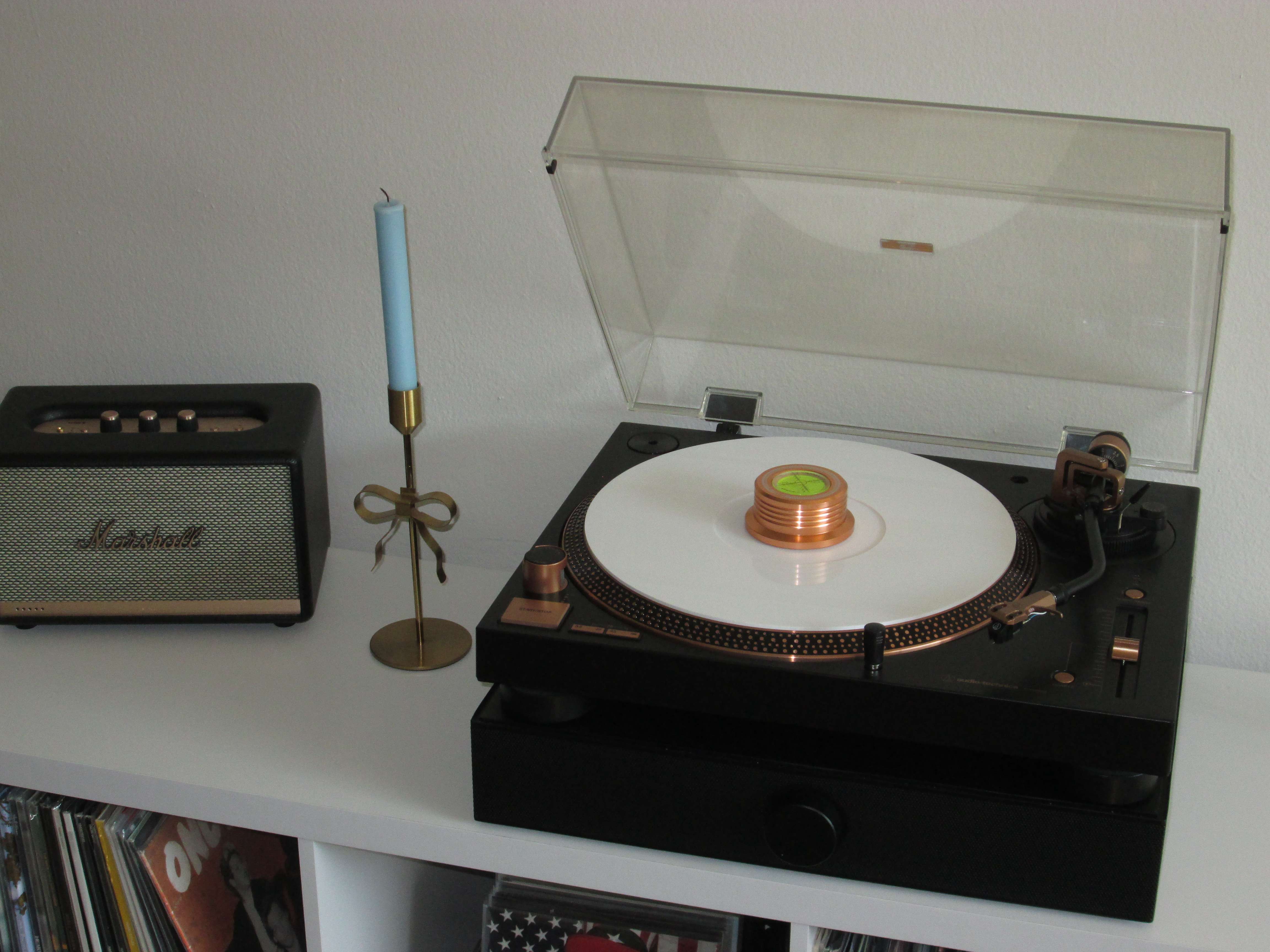 Close-up of Caroline’s bronze Audio-Technica LP120X turntable playing a white vinyl record with a Viborg record weight, next to a Marshall speaker and candle stand, displayed on a white cube organizer of records.