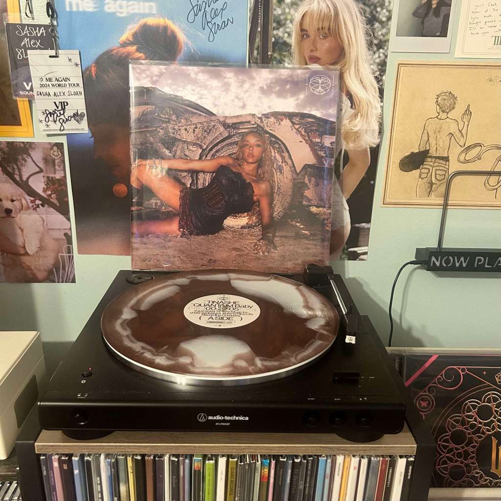 A brown-and-white swirl vinyl record spinning on an Audio-Technica LP60X turntable, with a cover art of a woman posing against industrial wreckage displayed behind it.