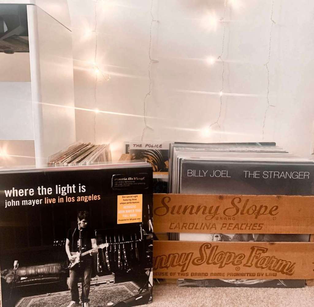 Wooden crates filled with vinyl records including John Mayer’s “Where the Light Is” and Billy Joel’s “The Stranger,” with string lights draped along the wall.