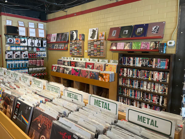 Interior of Breakaway Records, with rows of vinyl organized by genre, including a “Metal” section in the foreground. Album covers are displayed on the walls above, while shelves of CDs, cassettes, and accessories line the back. The space has a cozy, crate-digging atmosphere with a mix of new and used records.