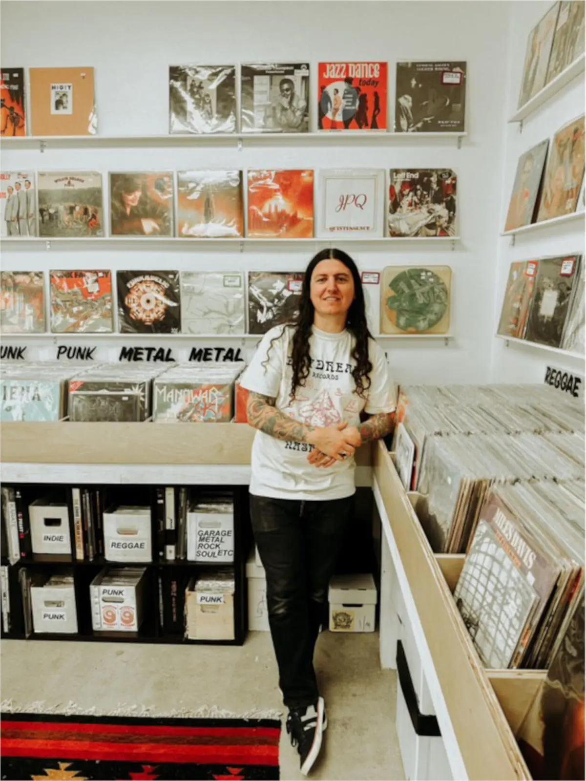 Person standing inside Daydream Records surrounded by vinyl bins, with neatly displayed records organized by genres like punk, metal, and reggae.