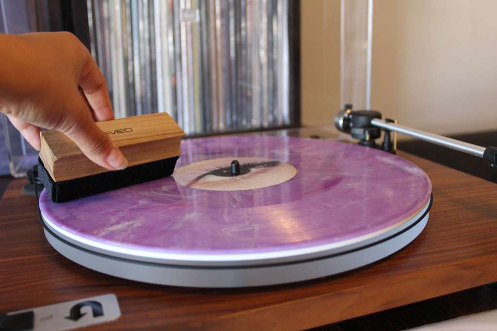Close-up of a hand cleaning a purple marbled vinyl record on a wooden turntable using a wooden record brush.