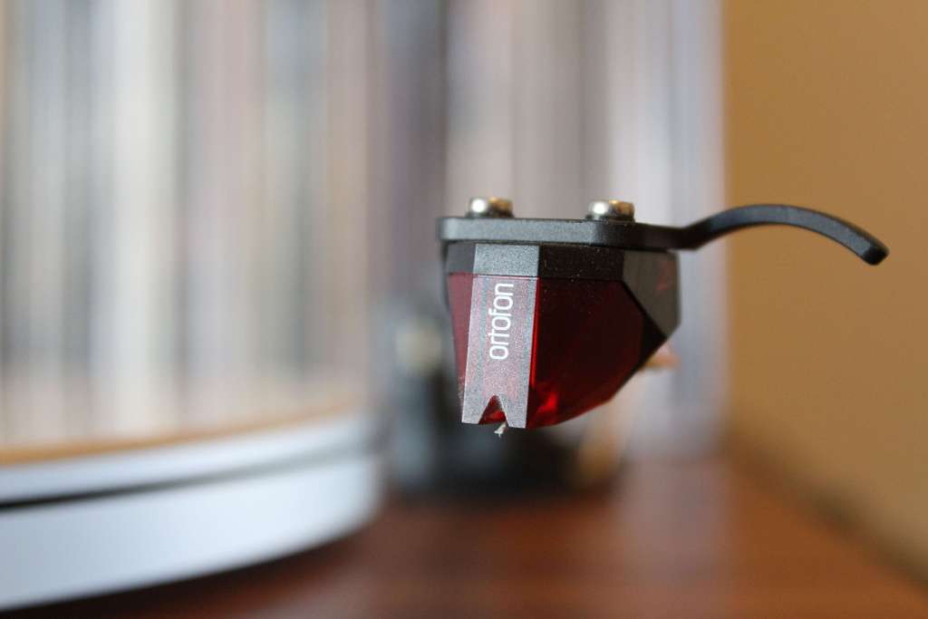 Macro shot of a red Ortofon turntable cartridge and stylus mounted on a tonearm.