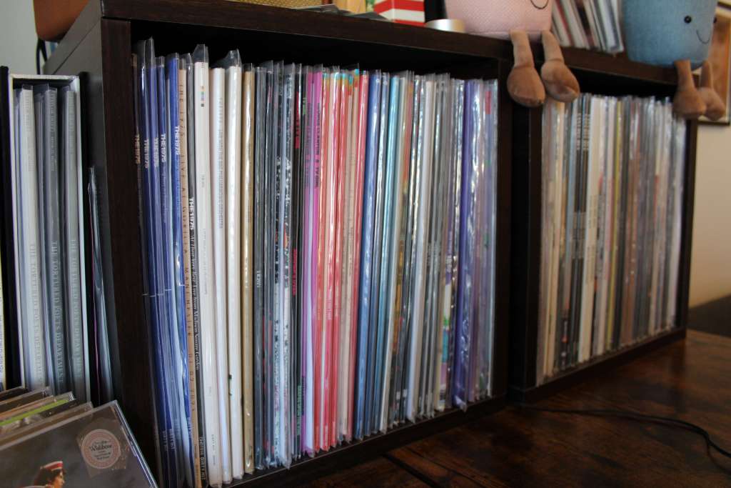 Wide view of a vinyl collection shelf with colorful spines visible, topped with plush plant pots and a Crosley record crate.