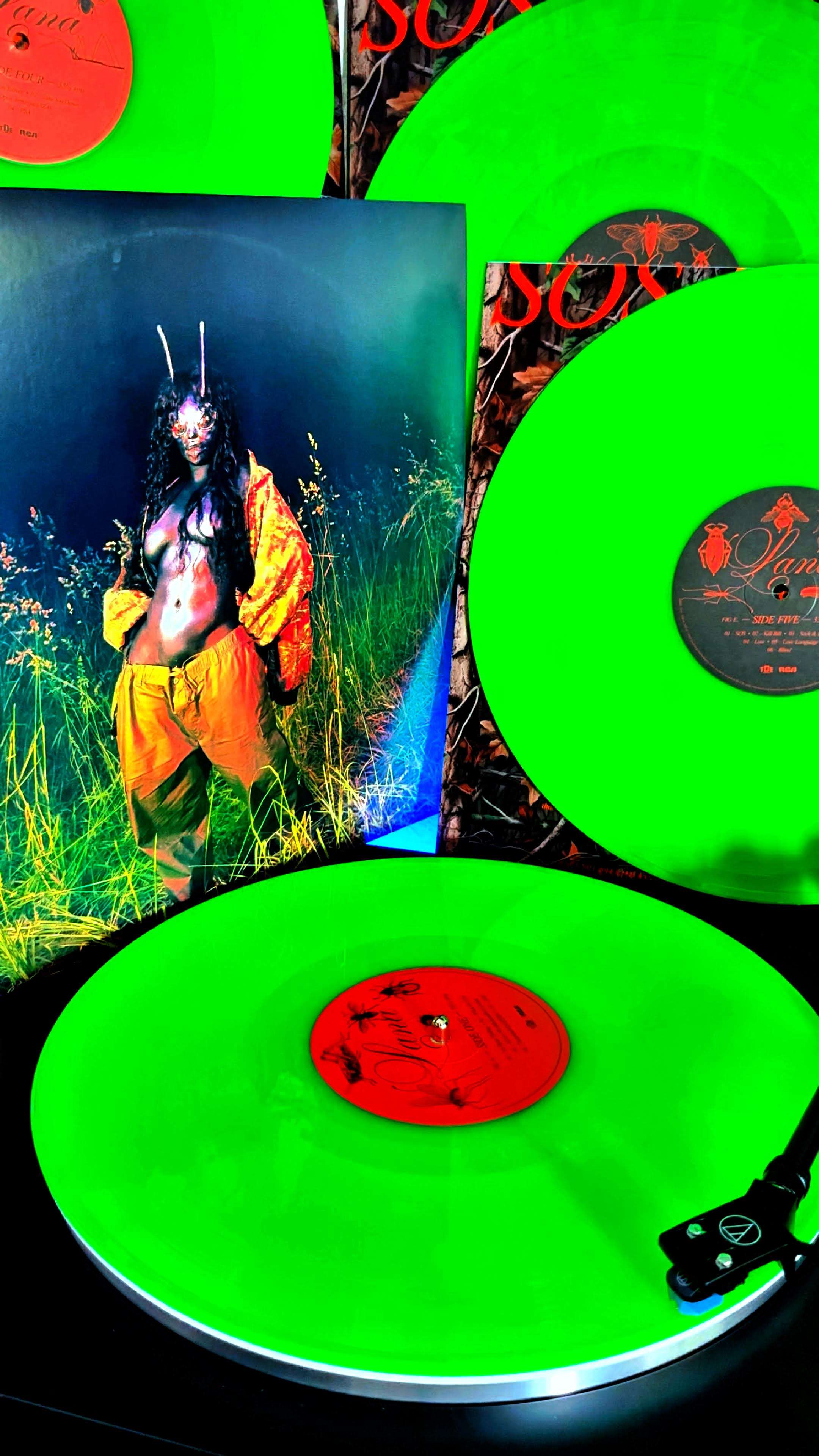 Neon green vinyl records by Dawn Richard displayed on a turntable and against their album cover, featuring a surreal portrait of the artist in a mask and orange jacket.