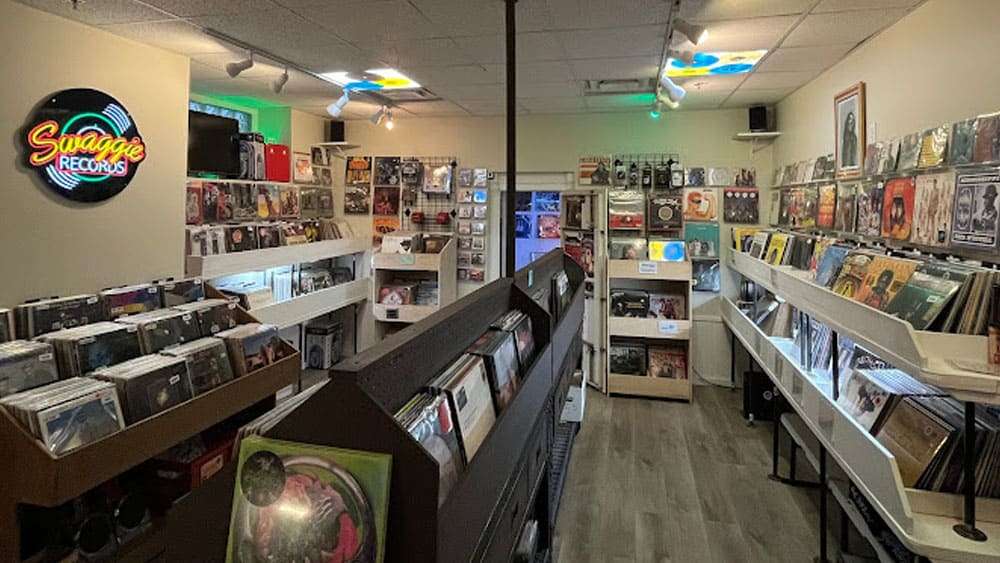 Interior of Swaggie Records with vinyl displayed along the walls, bins in the center, and a glowing neon sign that reads ‘Swaggie Records.