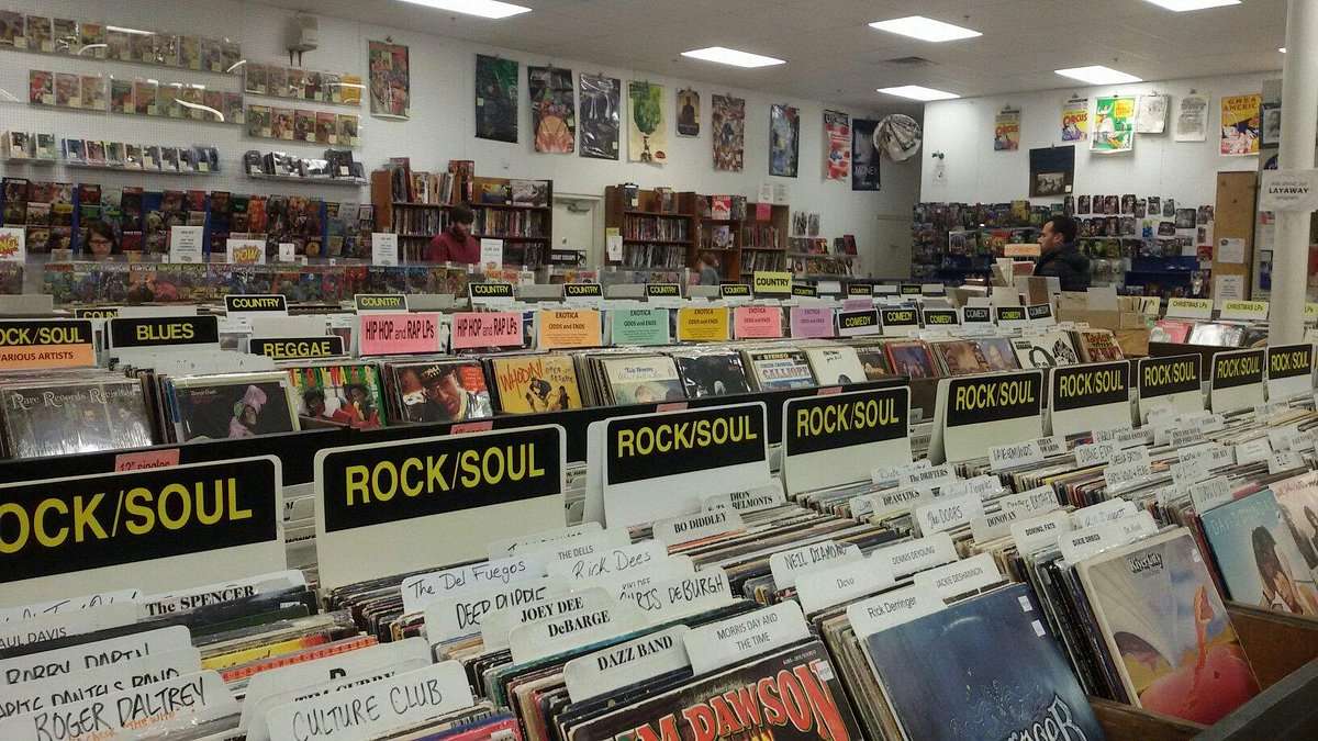 Interior of The Great Escape record store with aisles of vinyl and signs for genres like rock, soul, reggae, and hip hop, with walls lined with posters.
