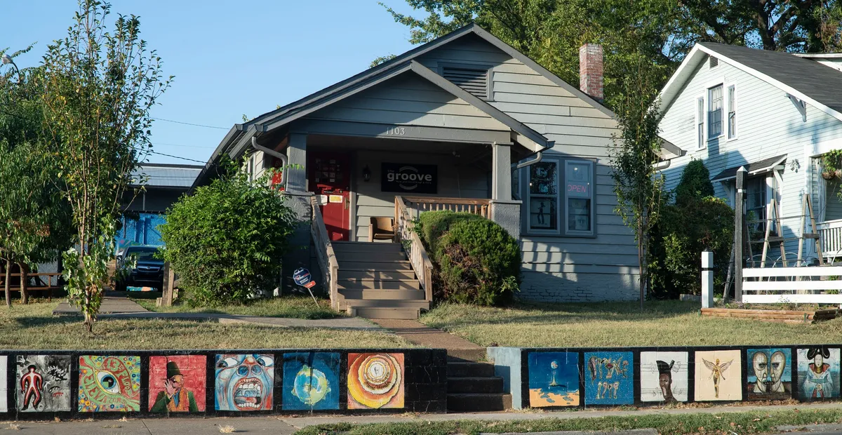 Exterior of The Groove record store in a small house with a front porch and colorful painted blocks featuring album art along the sidewalk.