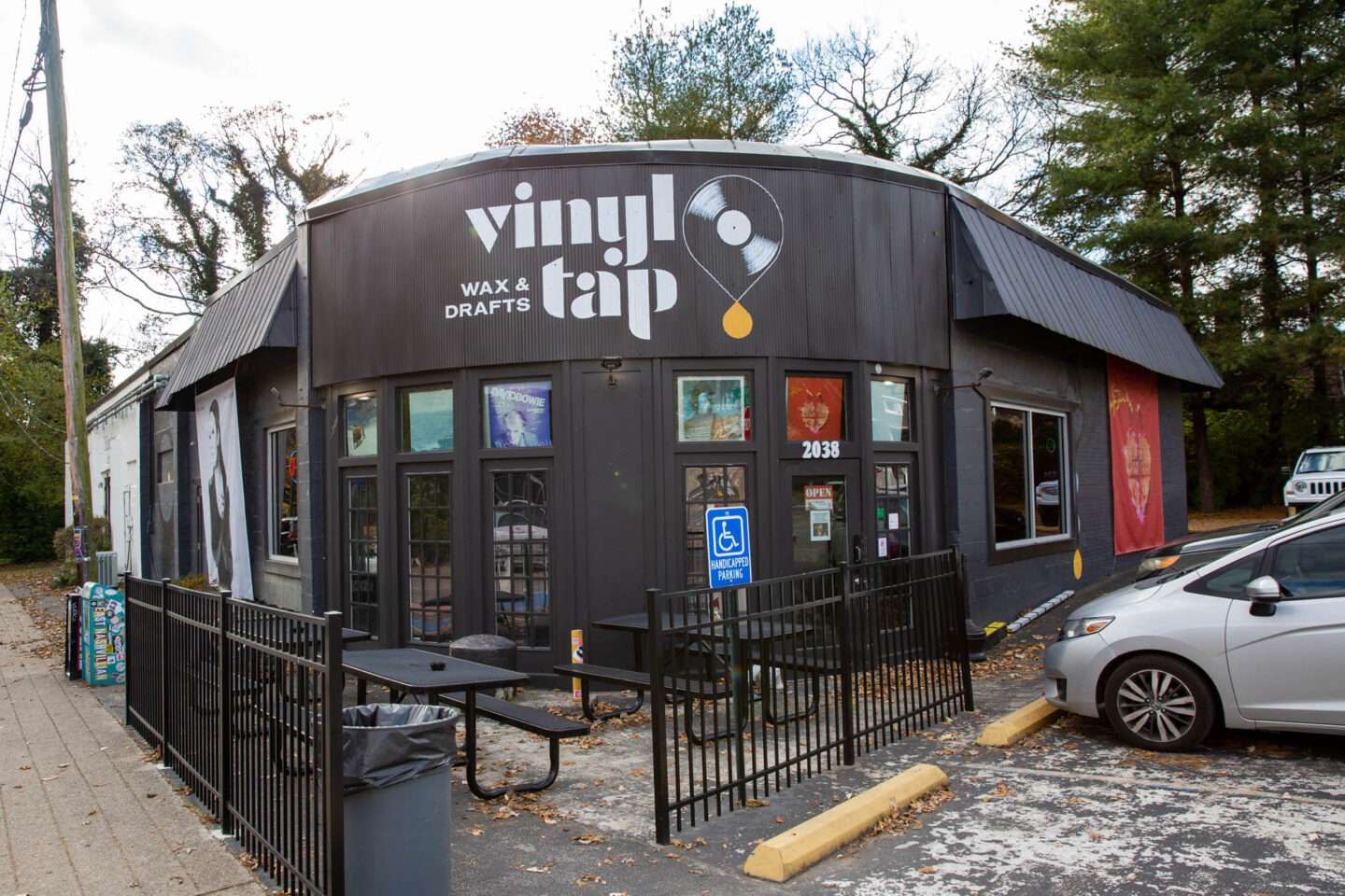 Exterior of Vinyl Tap, a record shop and bar with the tagline ‘Wax & Drafts’ painted on the building, with outdoor seating and a black facade.