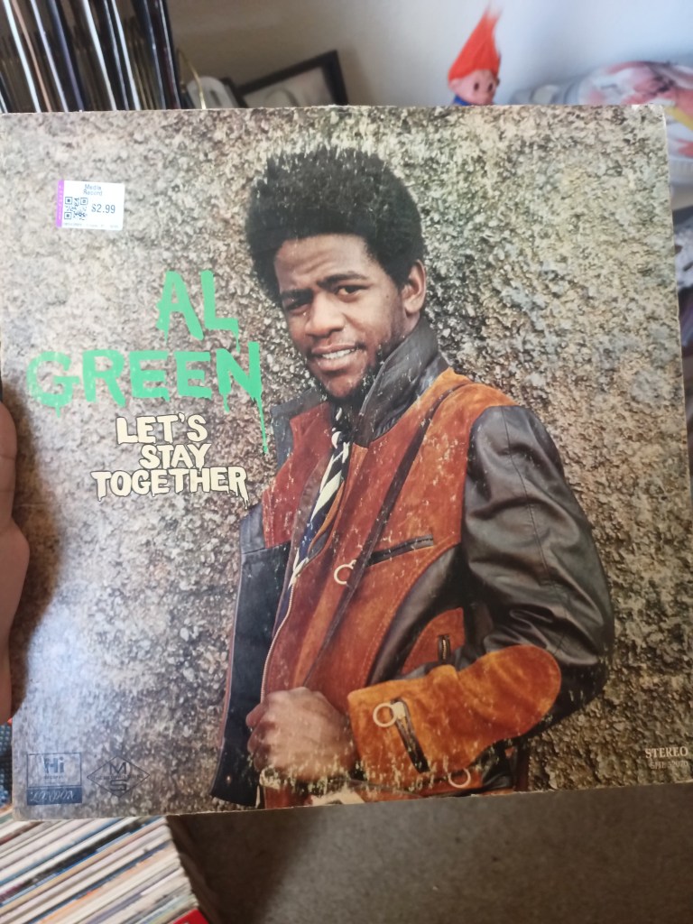 The cover of Let’s Stay Together by Al Green, showing him smiling in a brown and orange suede jacket against a rough stone wall background.