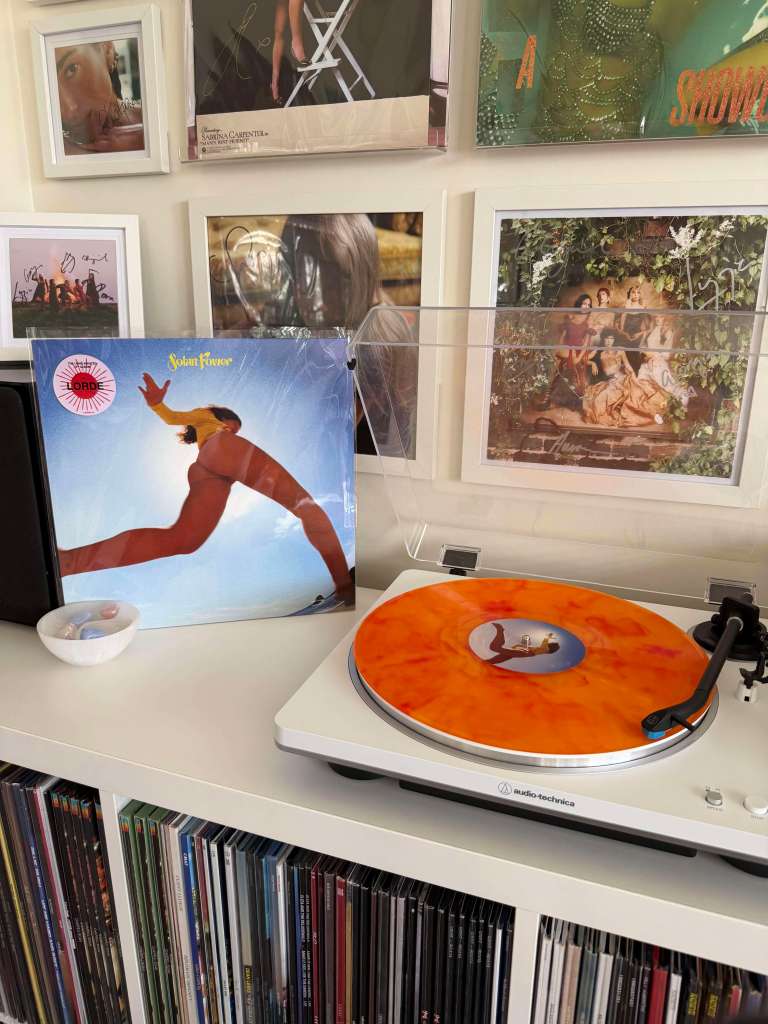 Lorde — “Solar Power” orange marbled LP playing on a white Audio-Technica turntable with framed art in the background.