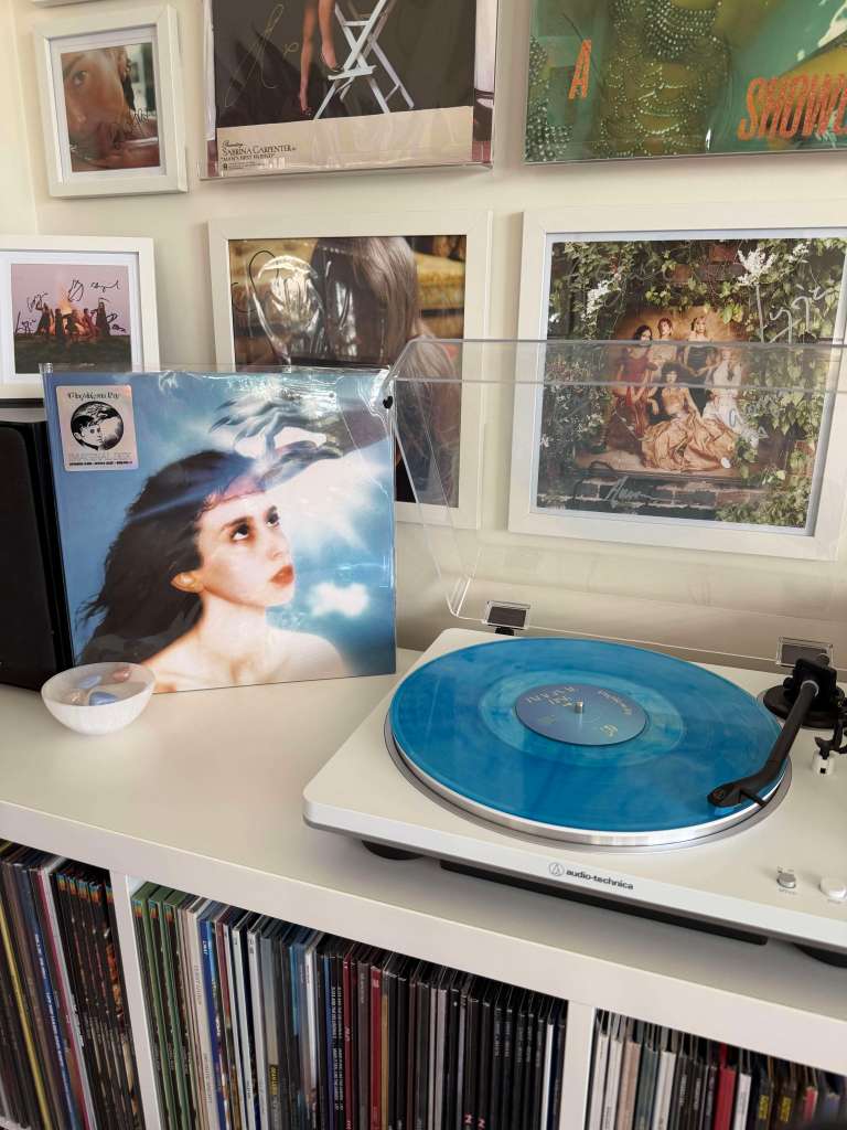 Caroline Polachek — “Magdalena Bay” transparent blue vinyl on a white Audio-Technica, surrounded by framed photos.