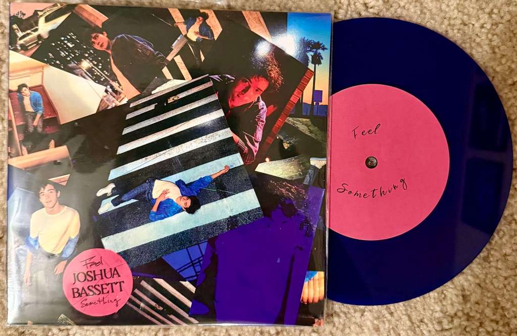 Joshua Bassett’s Feel Something vinyl showing a collage of photos of the artist and a blue record with a pink center label that reads “Feel Something.”