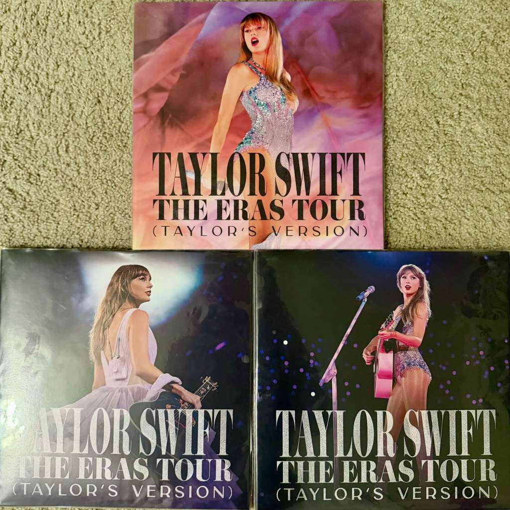 Three Taylor Swift “The Eras Tour (Taylor’s Version)” vinyl records displayed on beige carpet — one featuring Taylor in a glittering silver outfit and two showing her performing on stage with a microphone and guitar.