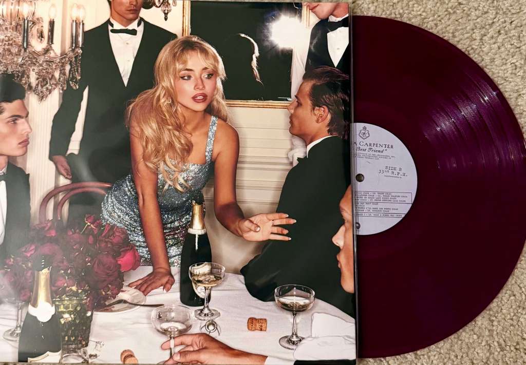 Sabrina Carpenter’s “Emails I Can’t Send” vinyl record featuring a glossy burgundy pressing beside a cover photo of Sabrina in a glamorous dinner party setting surrounded by champagne and guests in tuxedos.