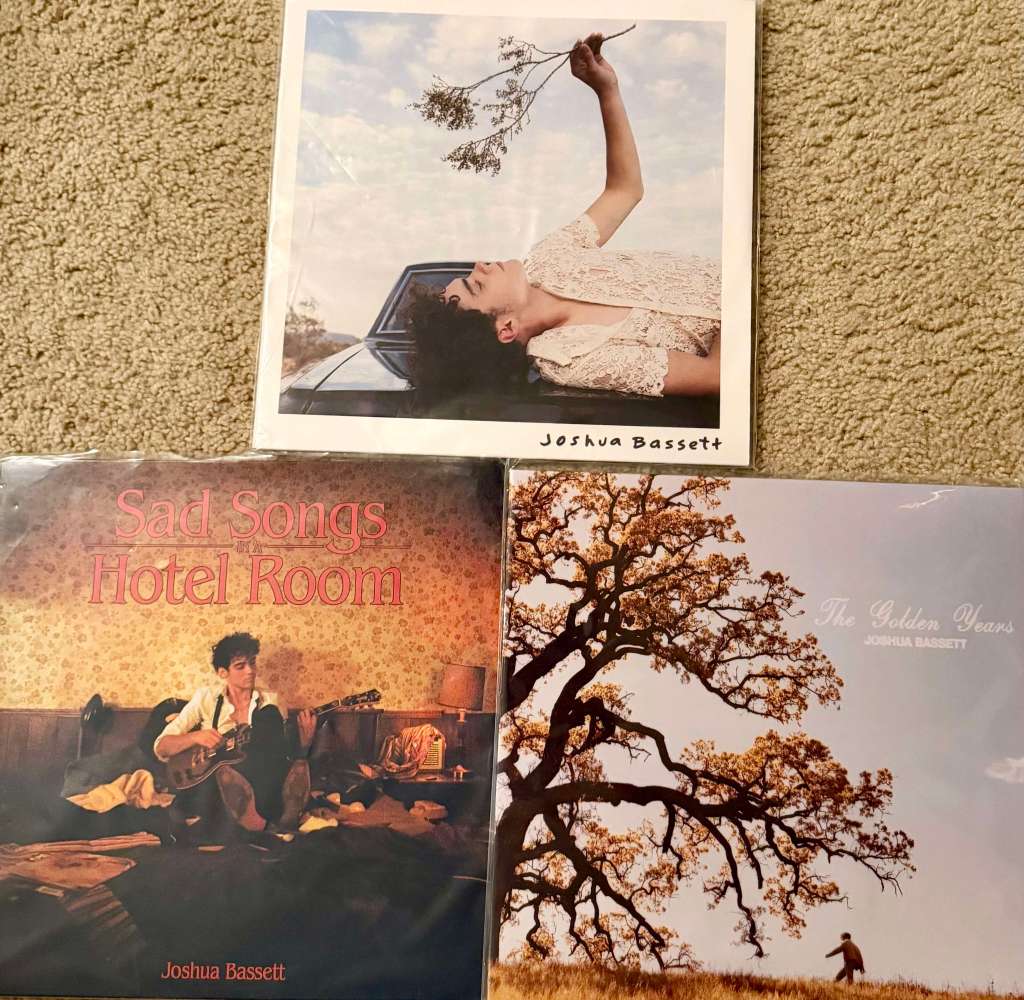 Three Joshua Bassett vinyl records — “Sad Songs in a Hotel Room,” “The Golden Years,” and his self-titled album — arranged neatly on a carpet, each featuring soft, nostalgic imagery.