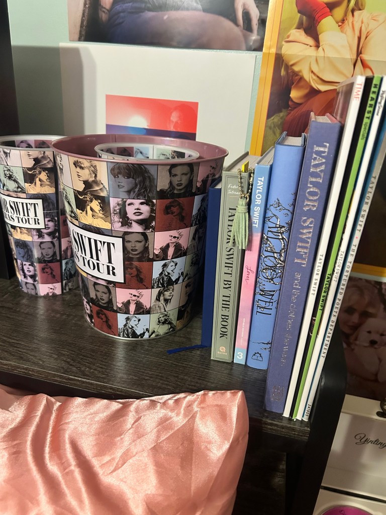 Matching Taylor Swift “The Eras Tour” popcorn bucket and cup on a wooden desk, decorated with album-era portraits in a collage design.