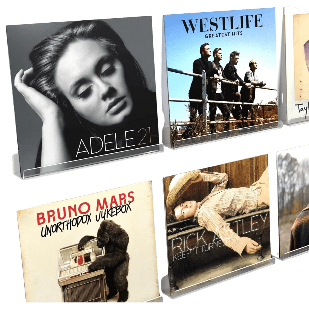A set of vinyl record sleeves displayed upright on clear acrylic stands. The visible albums include 21 by Adele, Greatest Hits by Westlife, Unorthodox Jukebox by Bruno Mars, and Keep It Turned On by Rick Astley. The transparent stands create a clean, floating effect that highlights each album cover’s artwork.