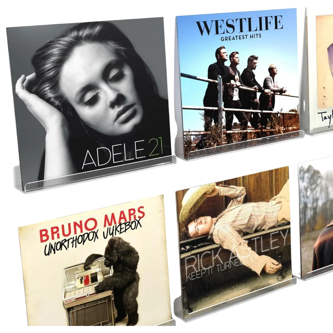 A set of vinyl record sleeves displayed upright on clear acrylic stands. The visible albums include 21 by Adele, Greatest Hits by Westlife, Unorthodox Jukebox by Bruno Mars, and Keep It Turned On by Rick Astley. The transparent stands create a clean, floating effect that highlights each album cover’s artwork.