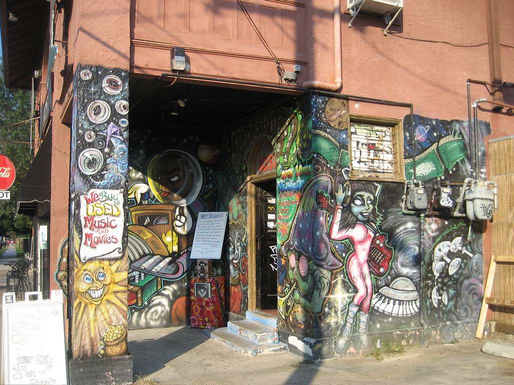 Exterior of The Mushroom record store in New Orleans, covered in colorful psychedelic murals and street art with a sign reading “We Buy Used Music and Movies.”