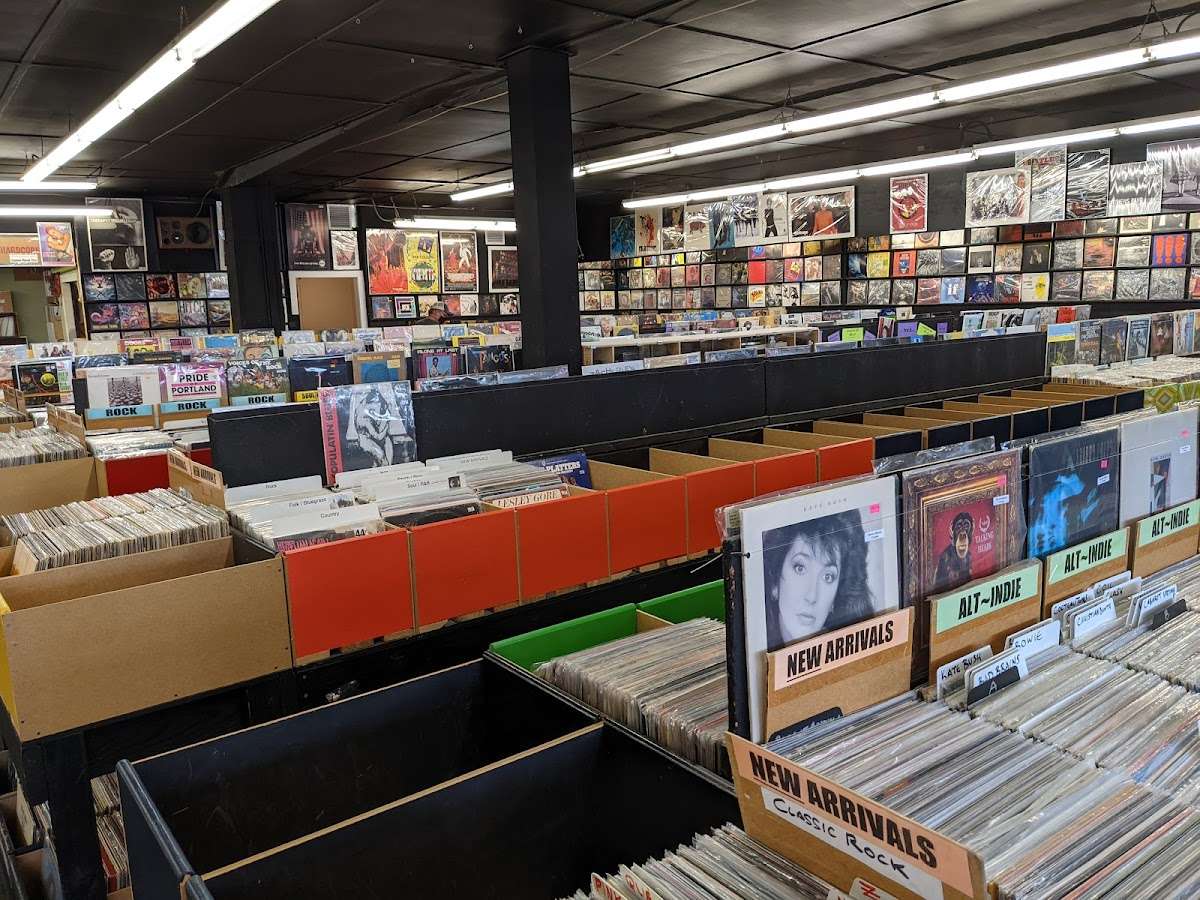 Interior view of Crossroads Music in Portland, Oregon, showing rows of record bins filled with vinyl across every genre, from alt-indie to classic rock. Album covers line the walls and ceiling, creating a cozy, crate-digger’s paradise with a vintage atmosphere.