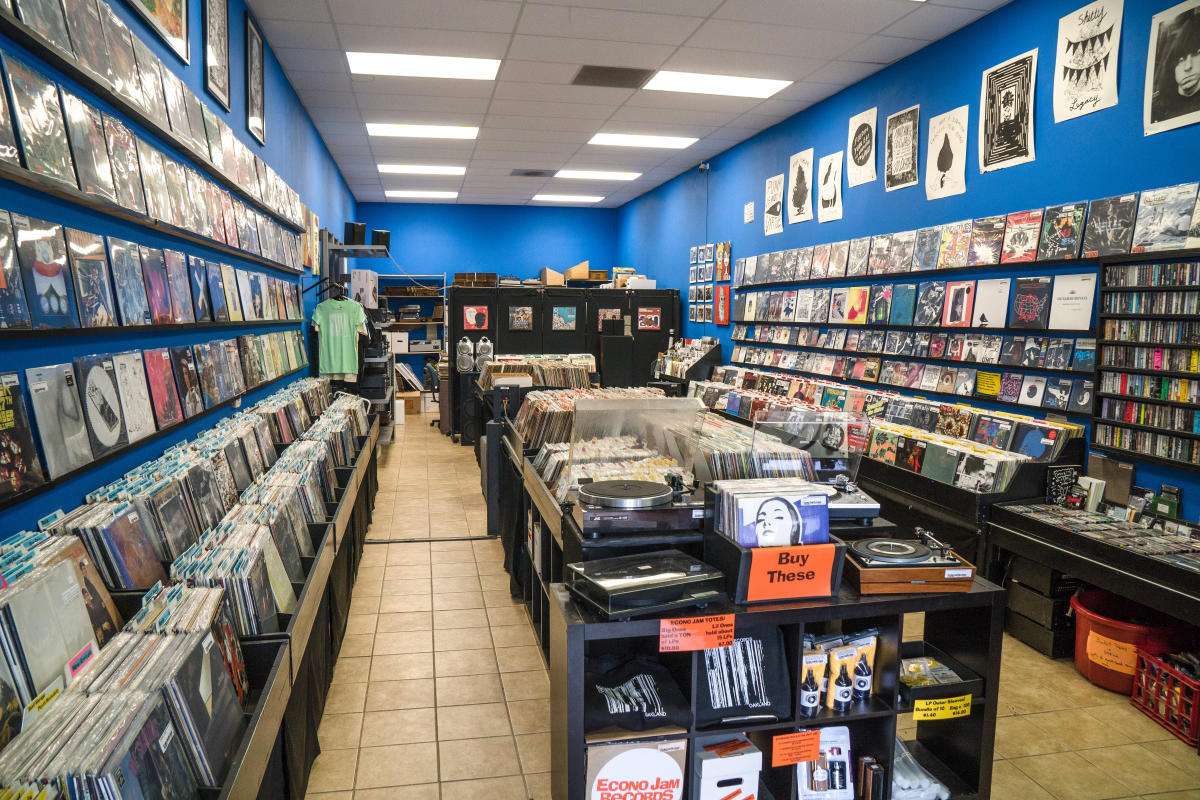 Oakland record store with long aisles of new/used vinyl, blue walls, and turntables on center table.