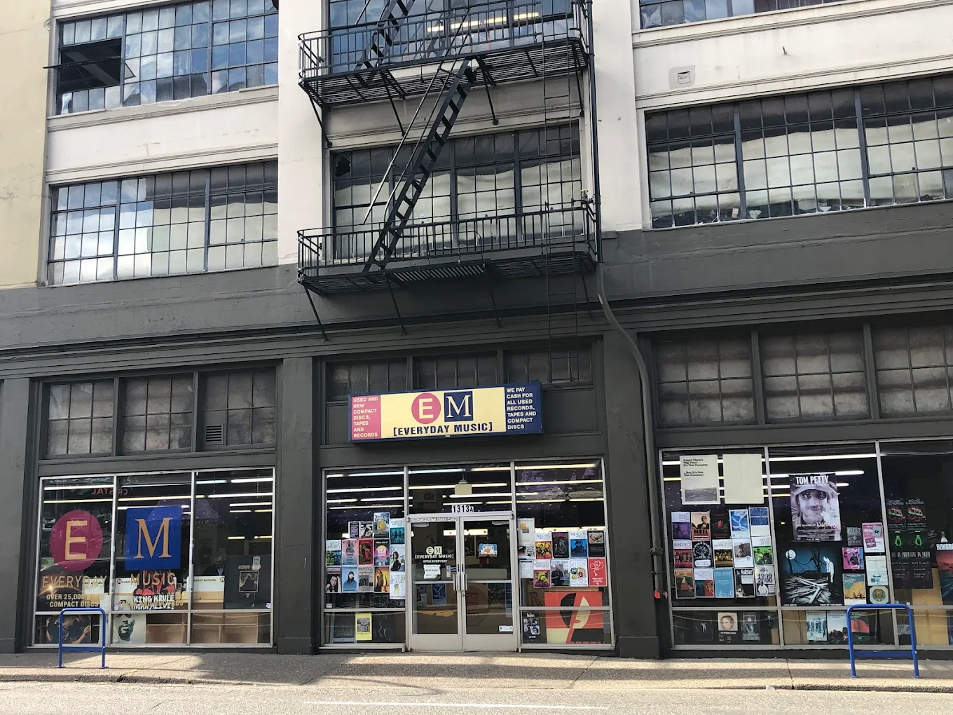 Exterior of Everyday Music in downtown Portland, Oregon, with large front windows displaying posters and album covers. The industrial-style building has tall glass panes, metal frames, and a sign that reads “Everyday Music – Used and New Compact Discs and Records.”