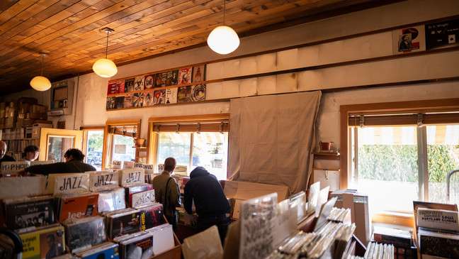 Inside Mississippi Records in Portland, Oregon, where customers browse through tightly packed bins of vinyl under warm lighting. The space has a rustic, homey charm with wooden ceilings and walls lined with album covers.