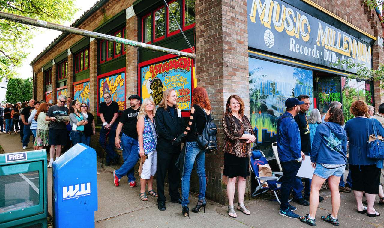 A long line of people waiting outside Music Millennium in Portland, Oregon, on Record Store Day. The brick building features colorful painted windows with phrases like “Keep Portland Weird” and “Sensational Selections,” capturing the excitement and community spirit of one of the city’s most iconic record stores.