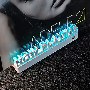 Acrylic “Now Playing” sign illuminated with blue LED light, holding the vinyl album Adele 21 upright on a dark textured surface.