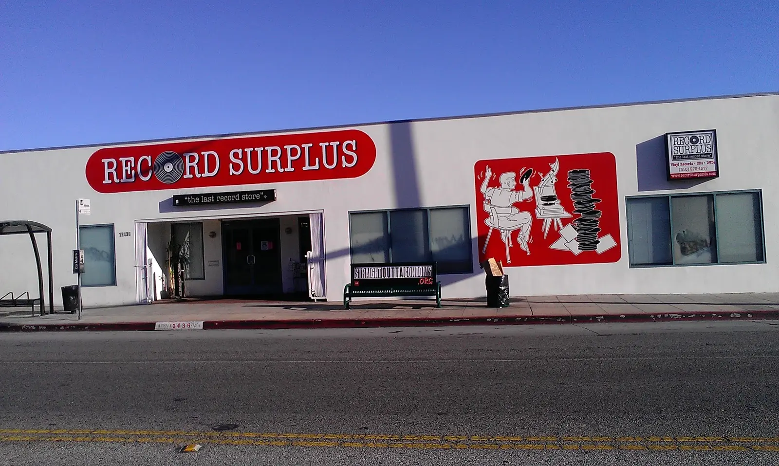 Exterior of Record Surplus in Los Angeles, featuring its signature red-and-white mural of a cartoon character surrounded by vinyl stacks. The shop’s tagline, “The Last Record Store,” is displayed above the entrance under a clear blue sky.