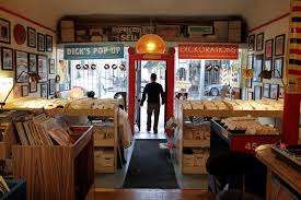 ozy vintage record shop in SF packed with 45s and LP bins, framed posters on the walls, and an open front door to the street.