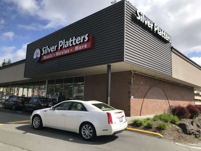Corner view of the Silver Platters storefront in a strip mall, large sign over glass windows with cars parked out front.