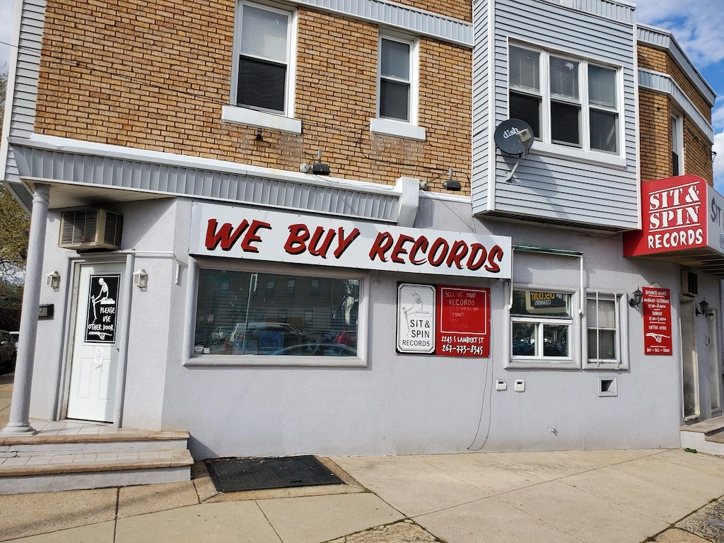Exterior of Sit & Spin Records in Philadelphia, a corner shop with a vintage sign reading “We Buy Records” and red awnings displaying the store name.