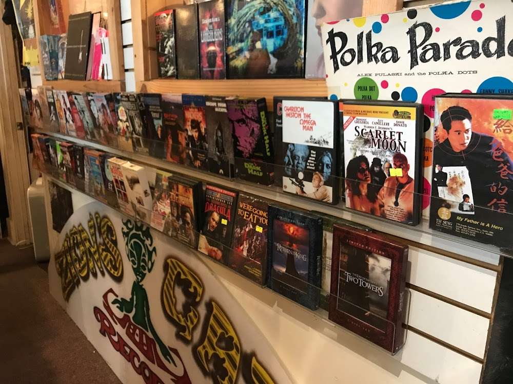 Counter and wall display packed with cult DVDs and vinyl sleeves inside Zion’s Gate, with hand-painted shop graphics.