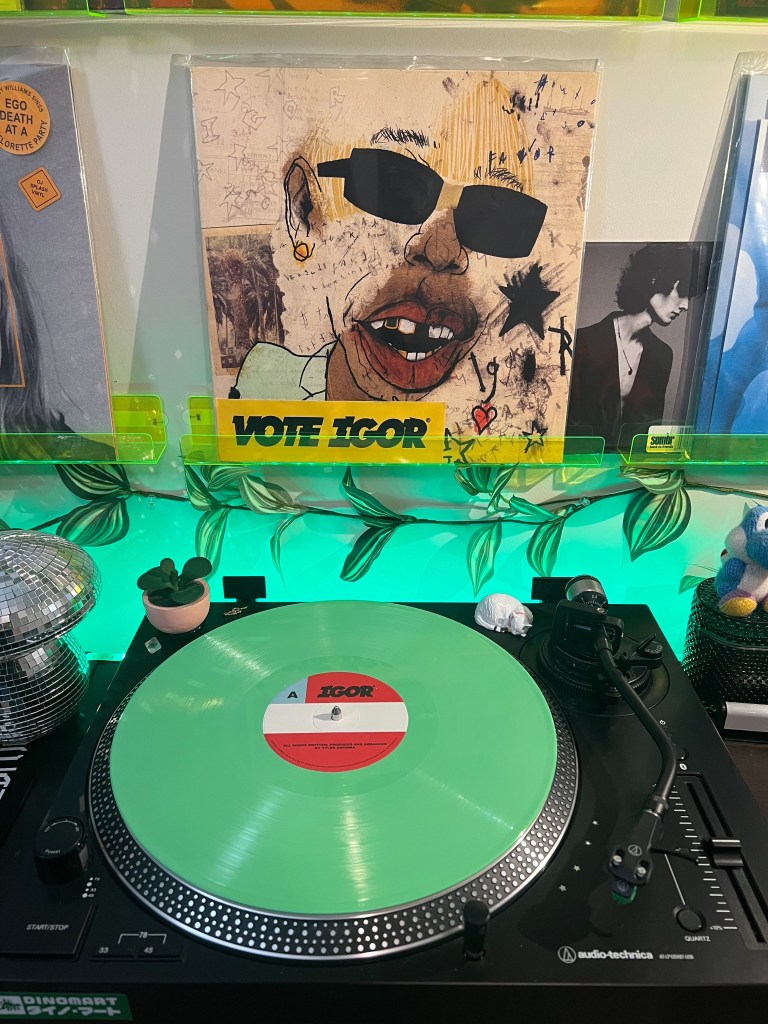 Solid green “IGOR” vinyl record on an Audio-Technica turntable, with Tyler, The Creator’s “Vote Igor” cover displayed above and green LED lighting with leaf graphics in the background.