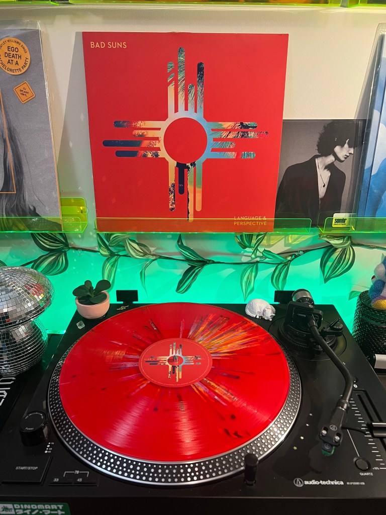 Red splatter vinyl on an Audio-Technica turntable beneath Bad Suns’ “Language & Perspective” album cover, framed by neon green acrylic shelving and leafy string decor.