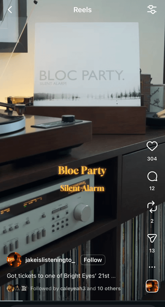Bloc Party “Silent Alarm” album cover displayed upright in a wooden vinyl record holder on a media console next to a turntable and hi-fi gear (Instagram Reel screenshot).