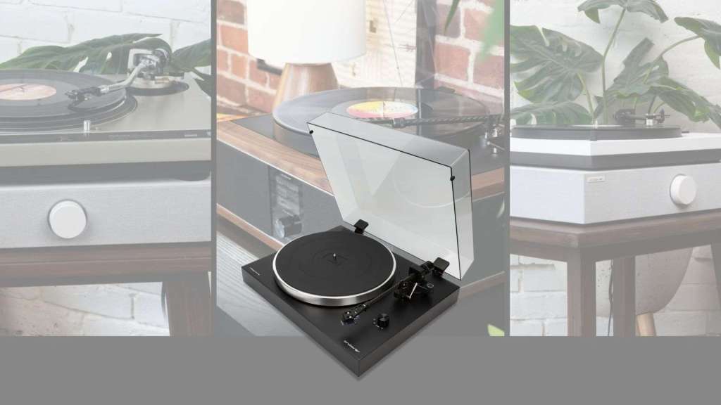 A black Andover Audio turntable with a silver-rimmed platter, tonearm, and an open clear dust cover sits in the center of a three-panel graphic. The center panel shows a record playing on a wood-trimmed turntable beside a lamp and brick wall. The faded side panels show a vintage silver turntable on the left and a white-and-gray Andover turntable on the right, both with leafy green plants behind them.