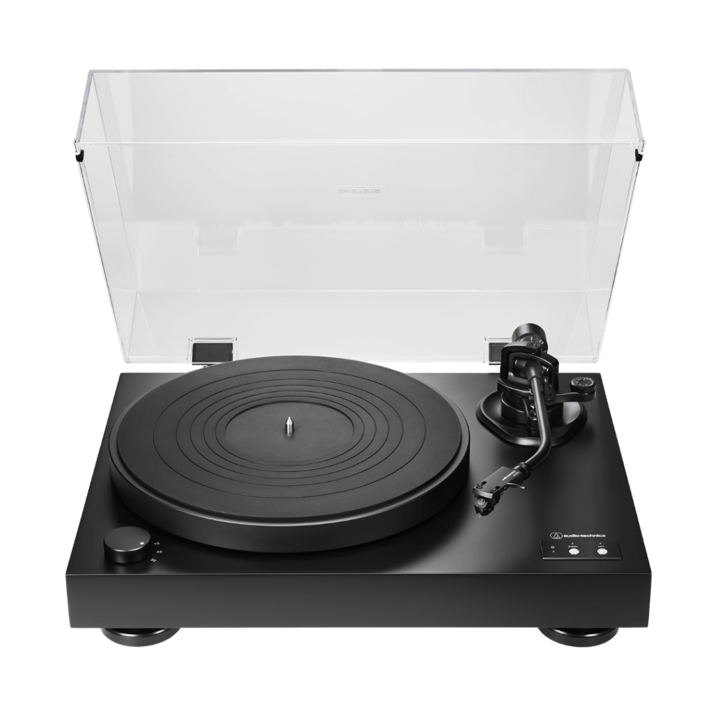 Top-down view of a matte black Audio-Technica turntable with a transparent acrylic dust cover propped open. The platter has a concentric-ring rubber mat and a silver center spindle. A black S-shaped tonearm with a headshell and cartridge sits on the right side. A round speed-selector knob (33, 45, 78) is at the lower left, and Start and Lift buttons are at the lower right. The base rests on two round black feet.